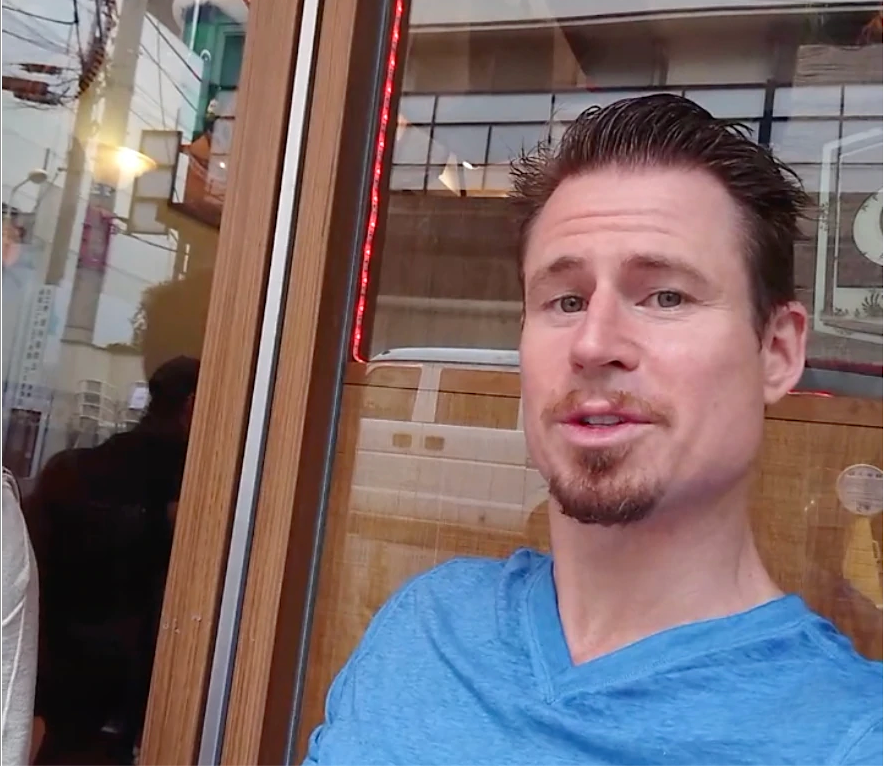 Karl G. client testimonial for Crack The Female Code dating course - man in blue t-shirt at outdoor cafe Japan